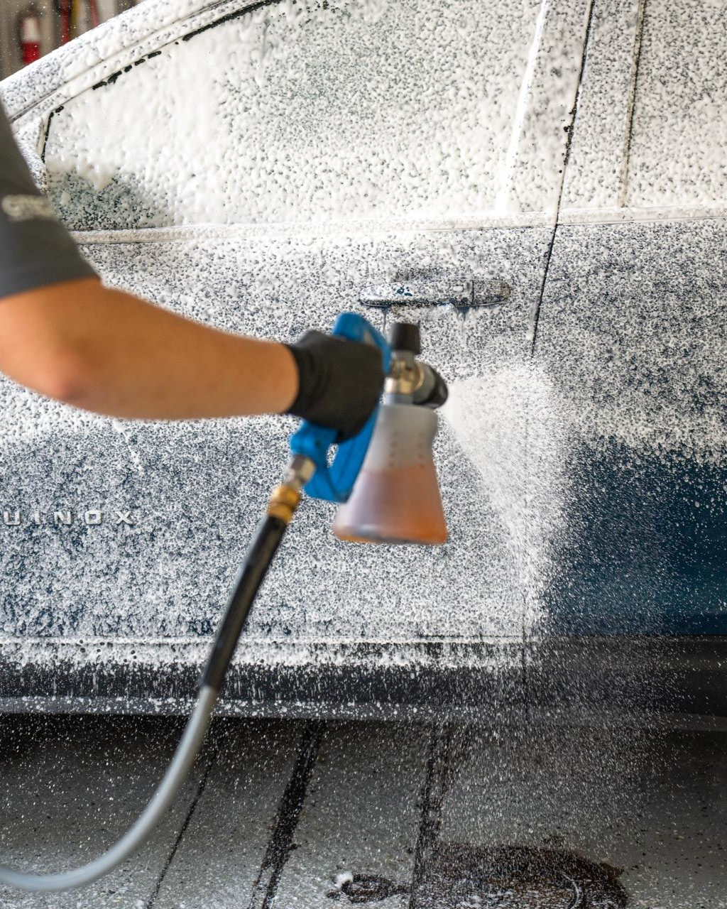 A car is being washed with a high pressure washer in a garage.