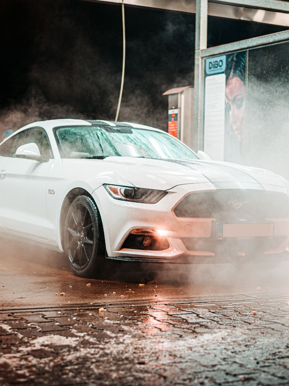 A car is being washed with a high pressure washer in a garage.