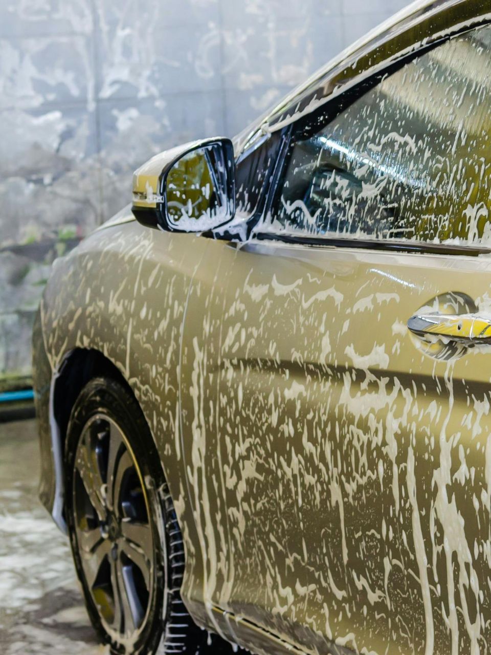 A car is being washed with a high pressure washer in a garage.