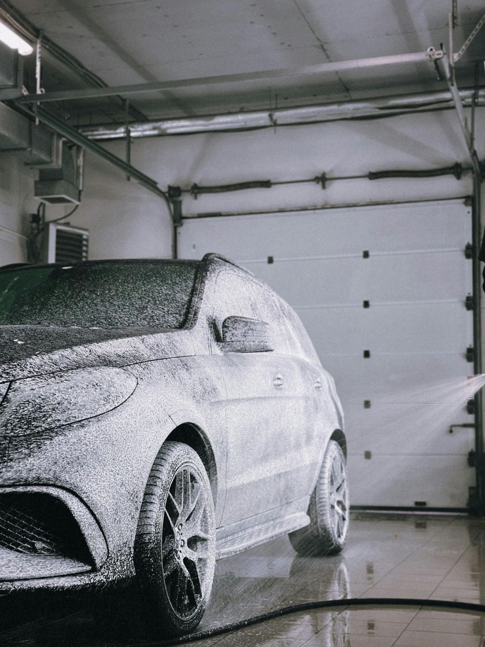 A car is being washed with a high pressure washer in a garage.