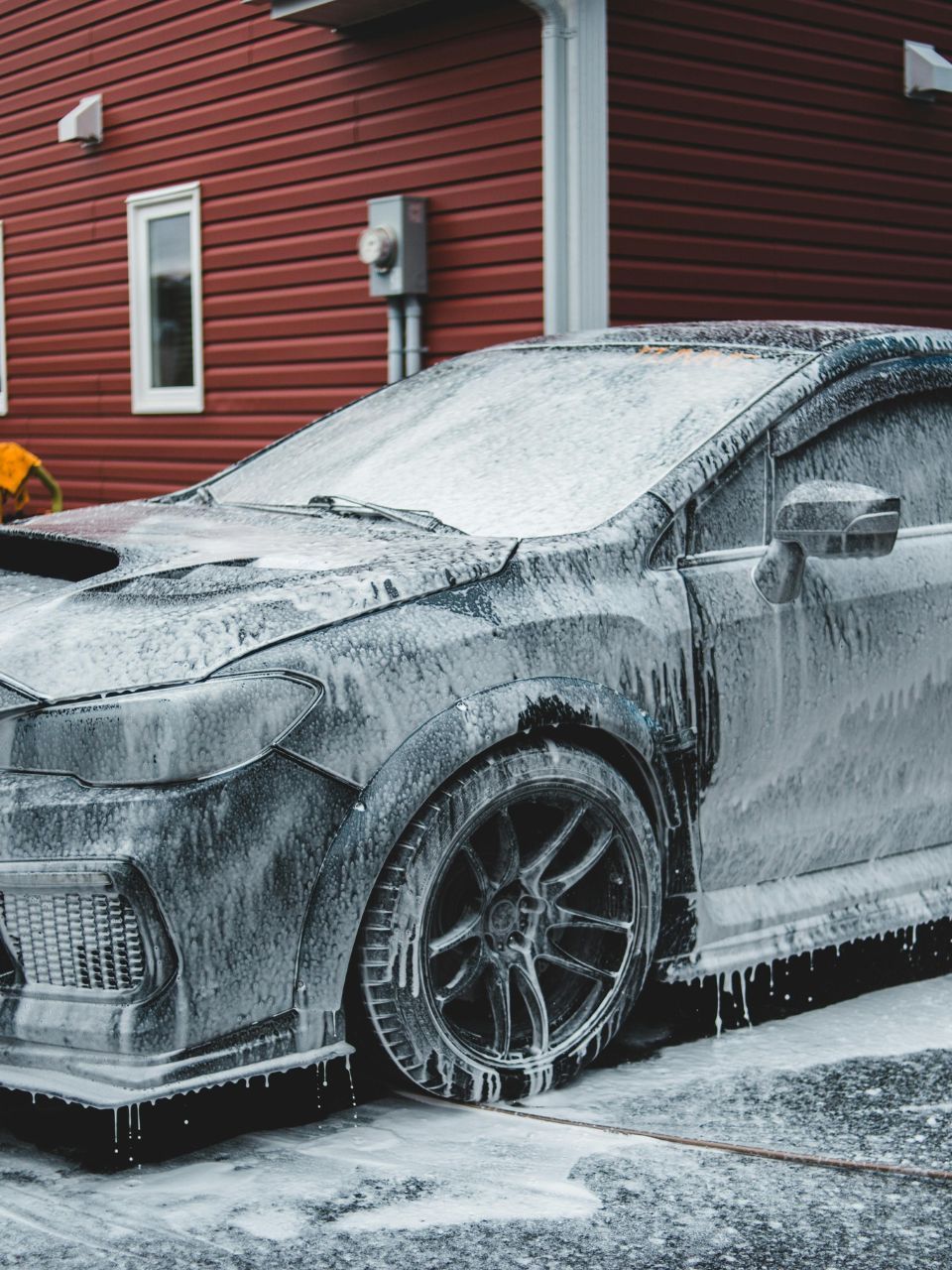 A car is being washed with a high pressure washer in a garage.