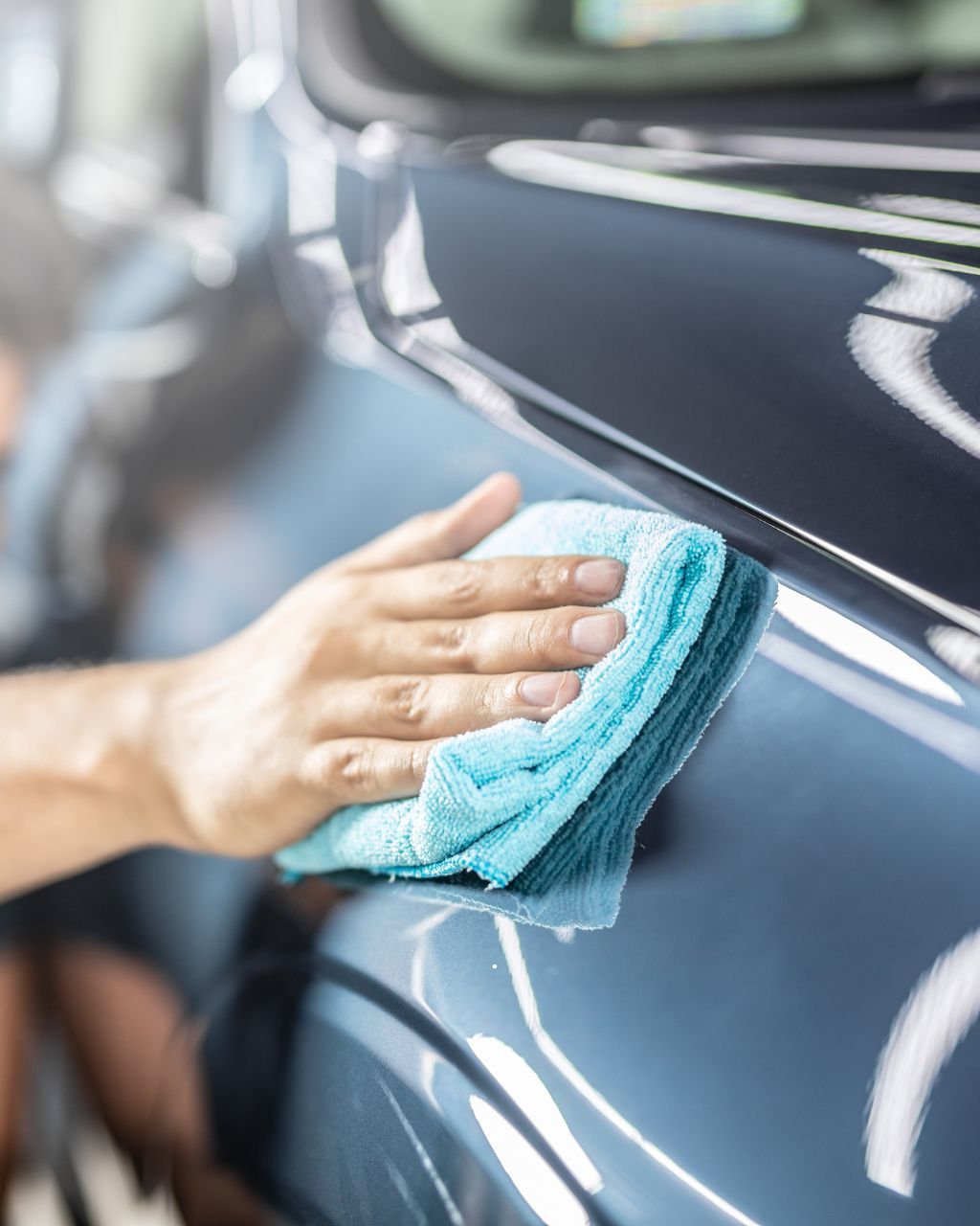 A person uses a pressure washer to clean the tire of a silver car inside a workshop with other vehicles.