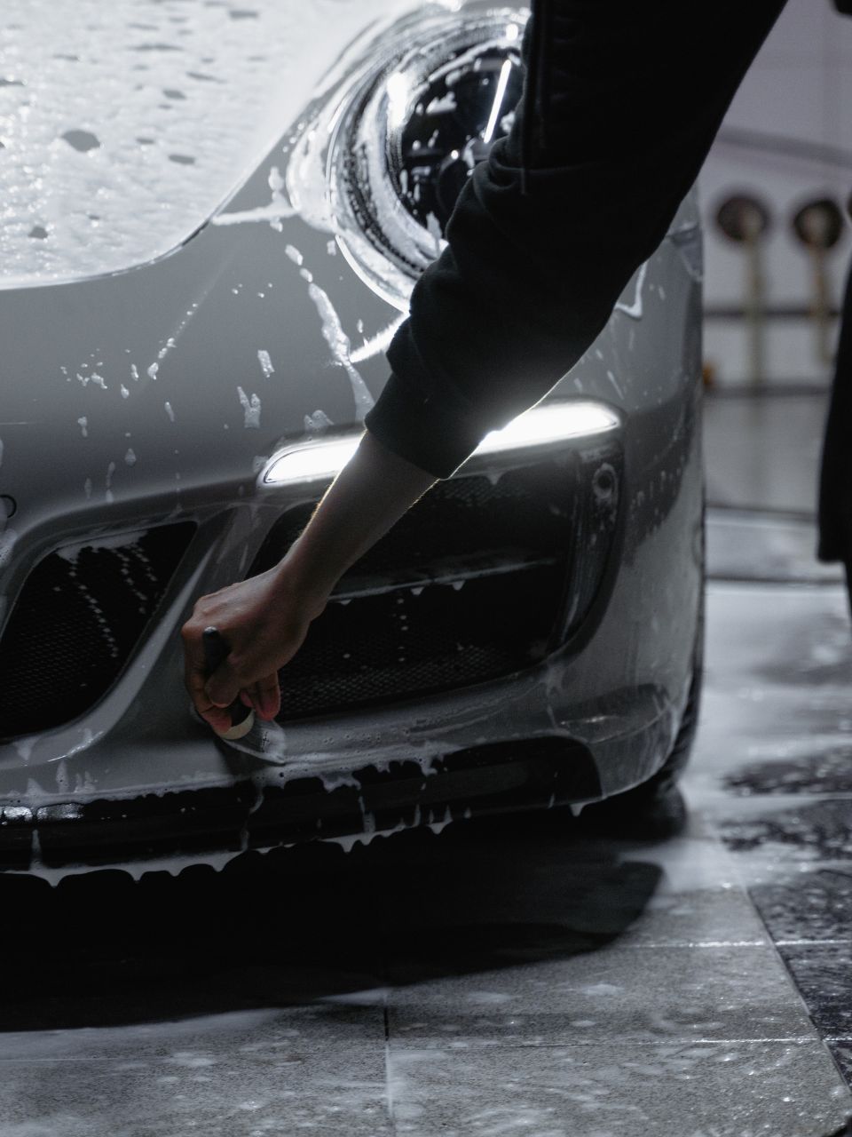 A car is being washed with a high pressure washer in a garage.