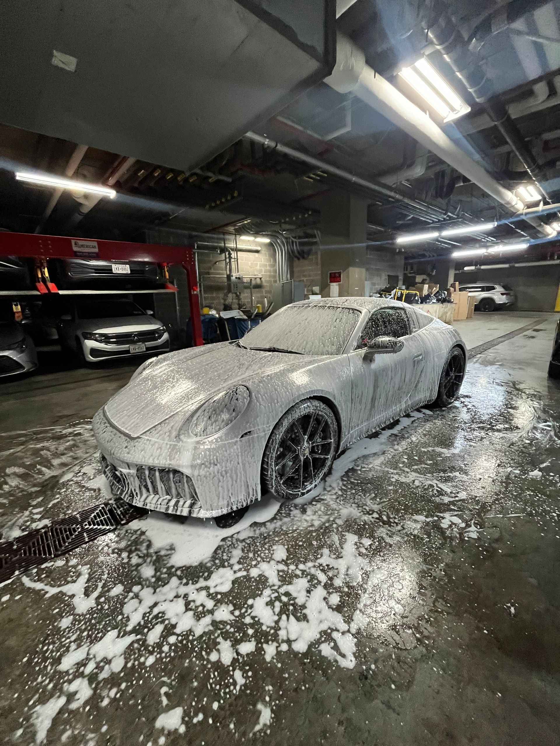 A car is being washed with a high pressure washer in a garage.