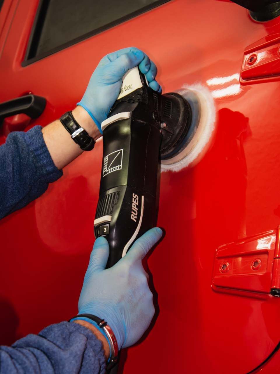 A car is being washed with a high pressure washer in a garage.