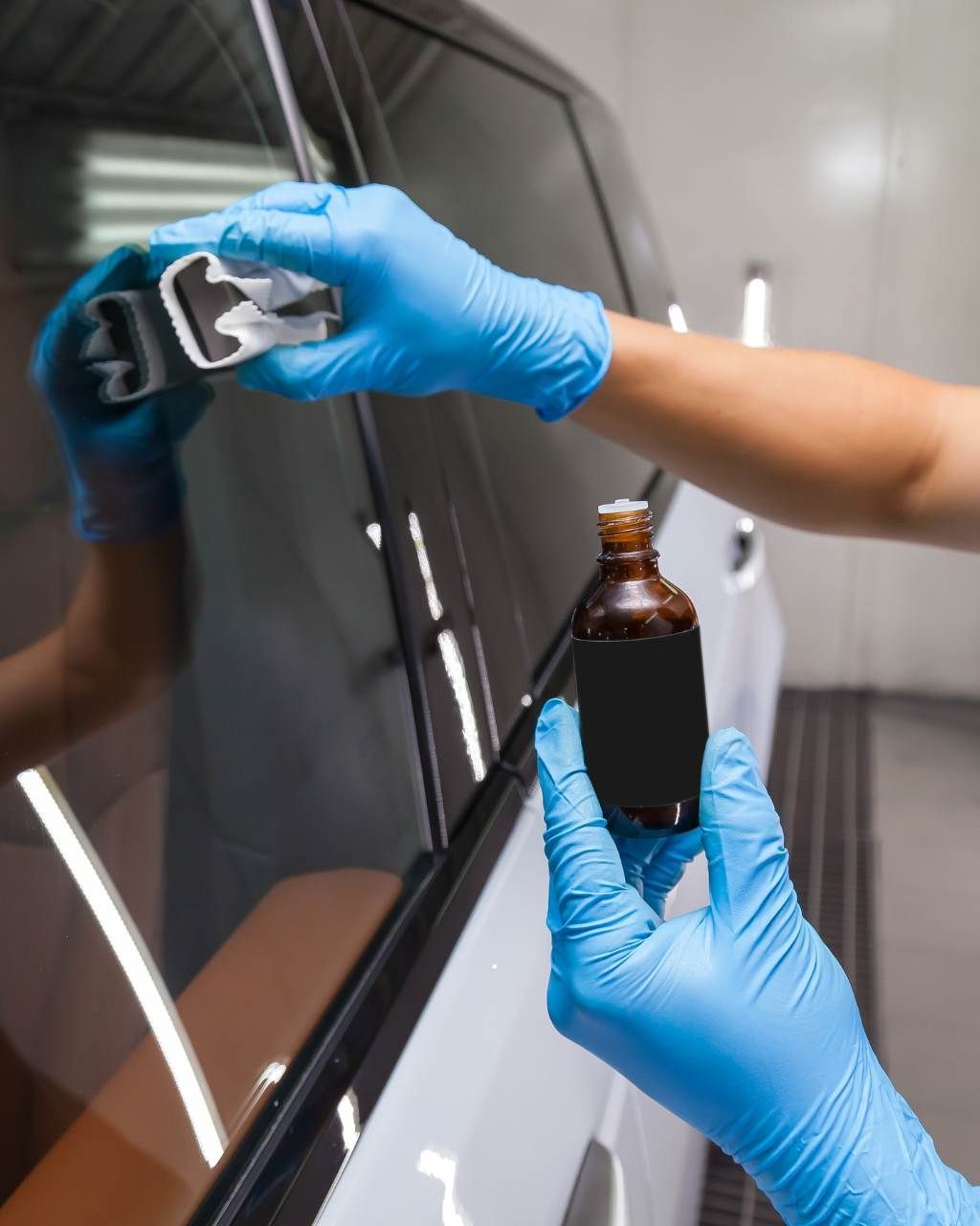 A detailer in a black uniform and cap uses a foam-covered mitt to wash a soap-covered car in a garage.