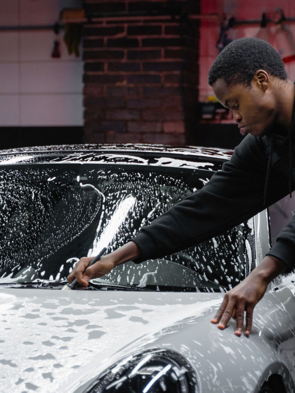 A car is being washed with a high pressure washer in a garage.