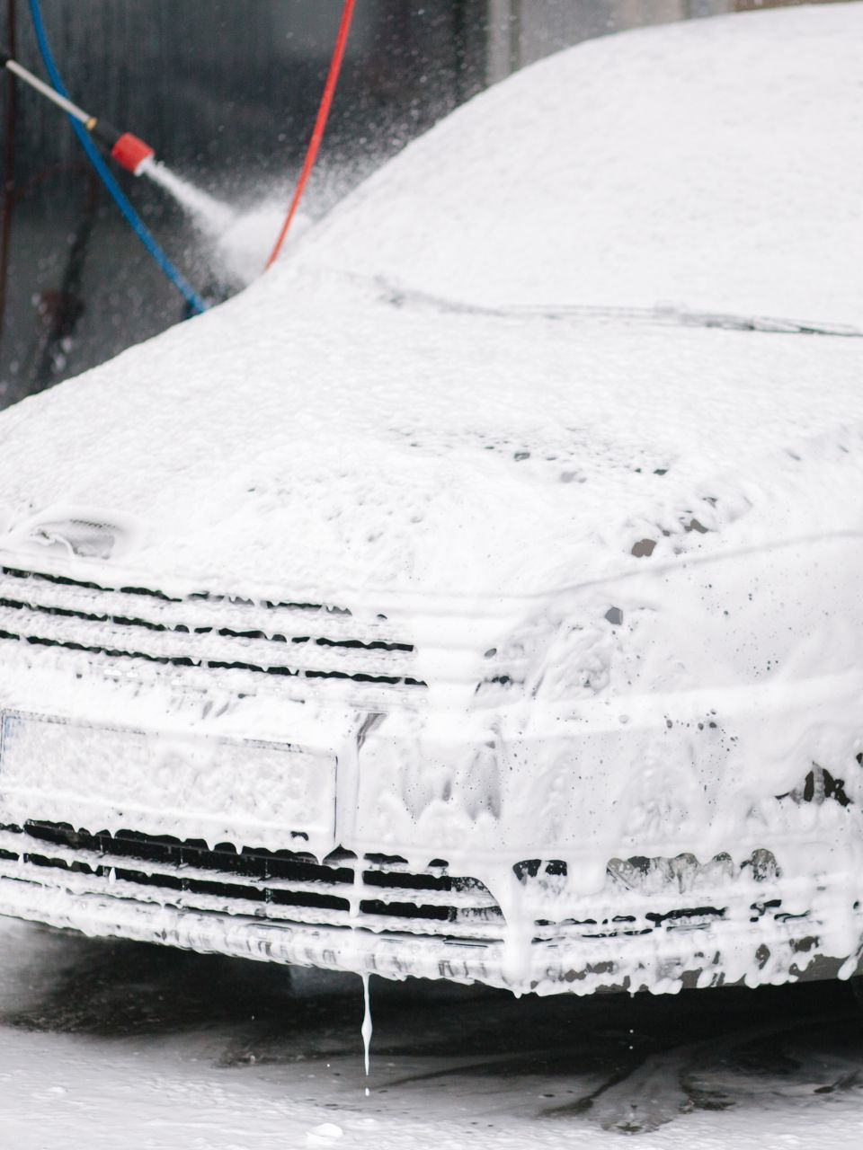 A car is being washed with a high pressure washer in a garage.