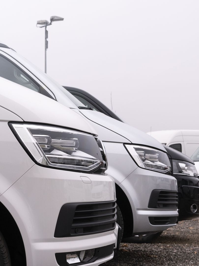 A row of white vans are parked next to each other in a parking lot.