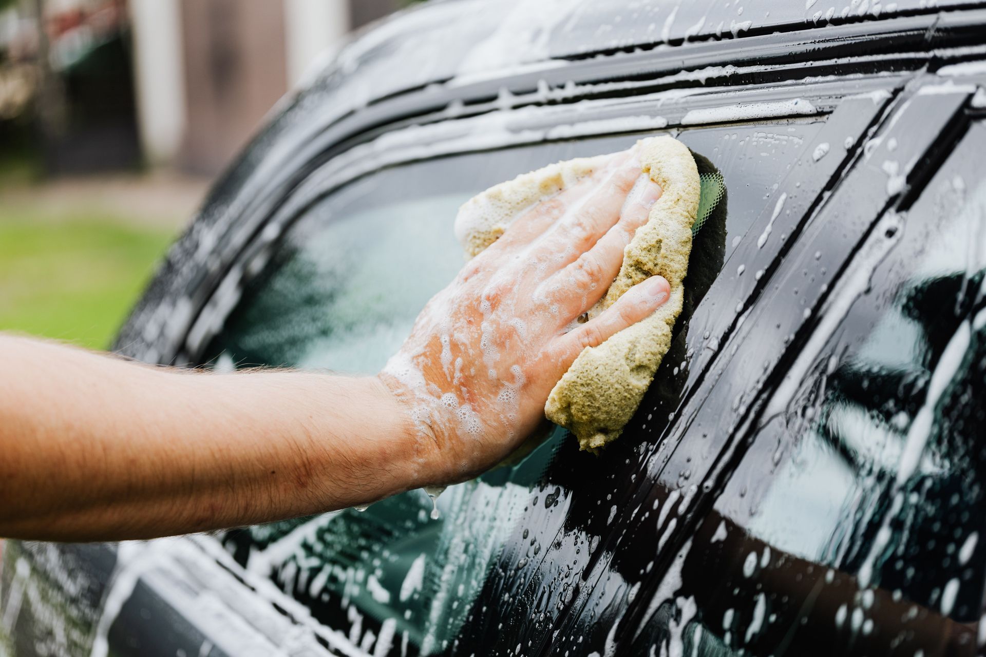 A person uses a pressure washer to clean the tire of a silver car inside a workshop with other vehicles.