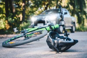 A bicycle and helmet are laying on the road in front of a car.