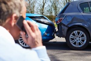 A man is talking on a cell phone in front of a car accident.