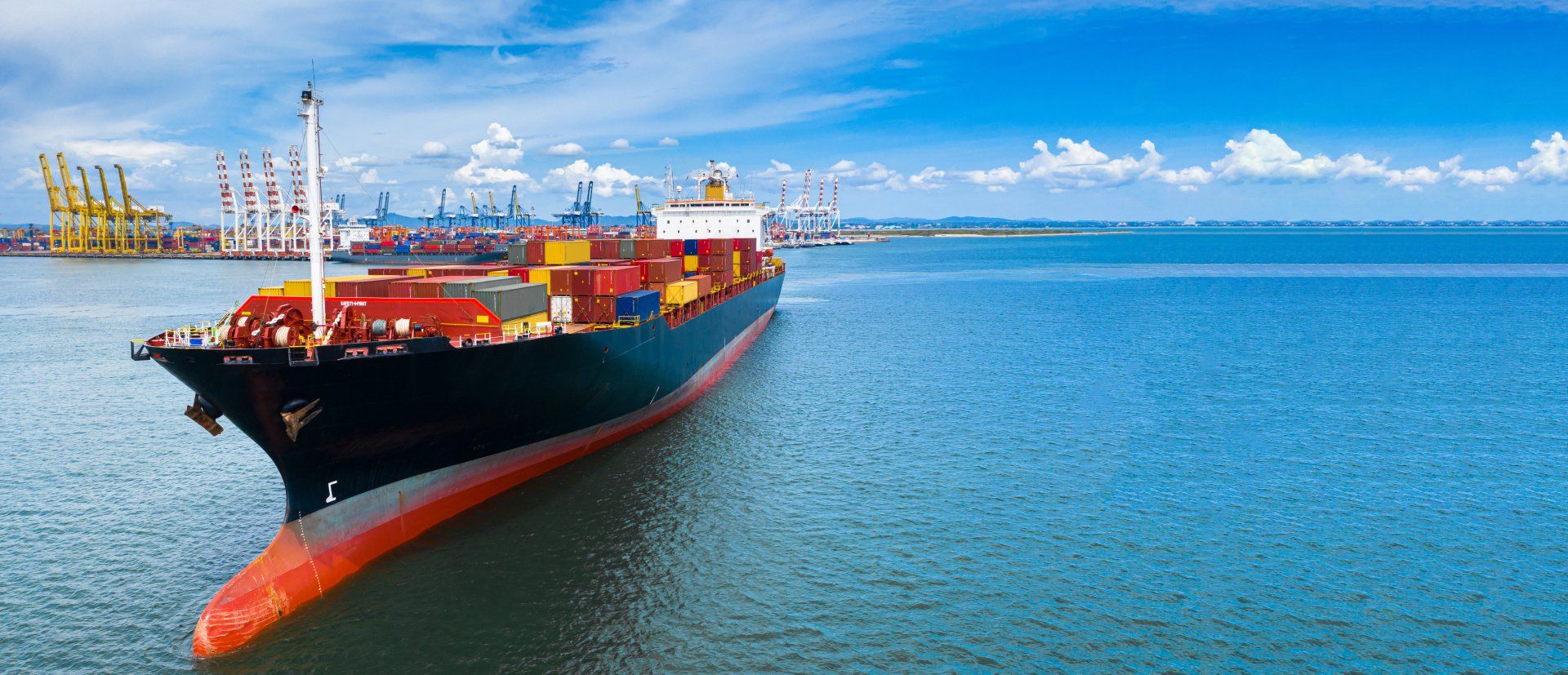 Cargo ship in the ocean near a port on a sunny day.