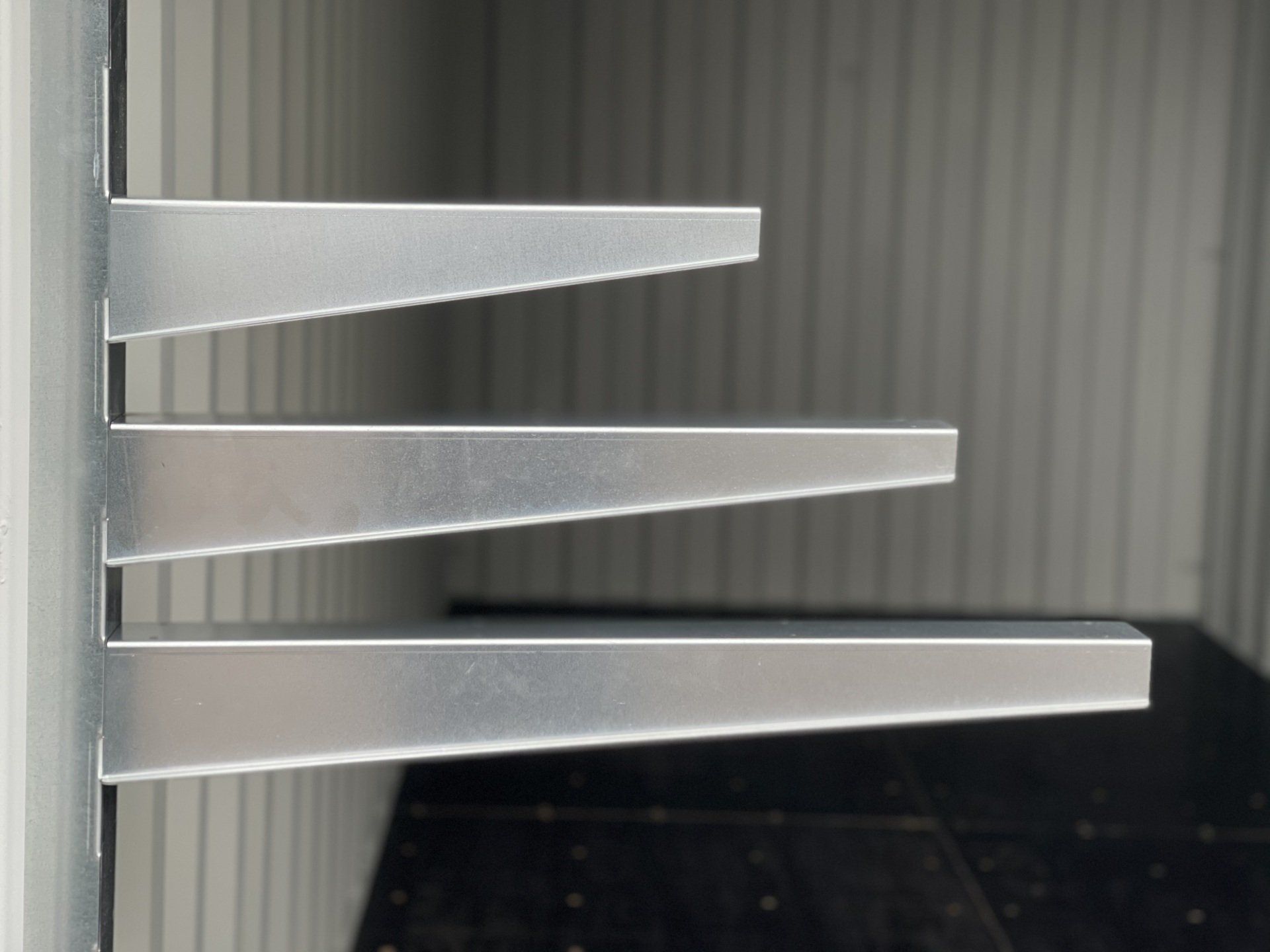 Three metal shelves mounted on a wall; the shelves gradually increase in length.