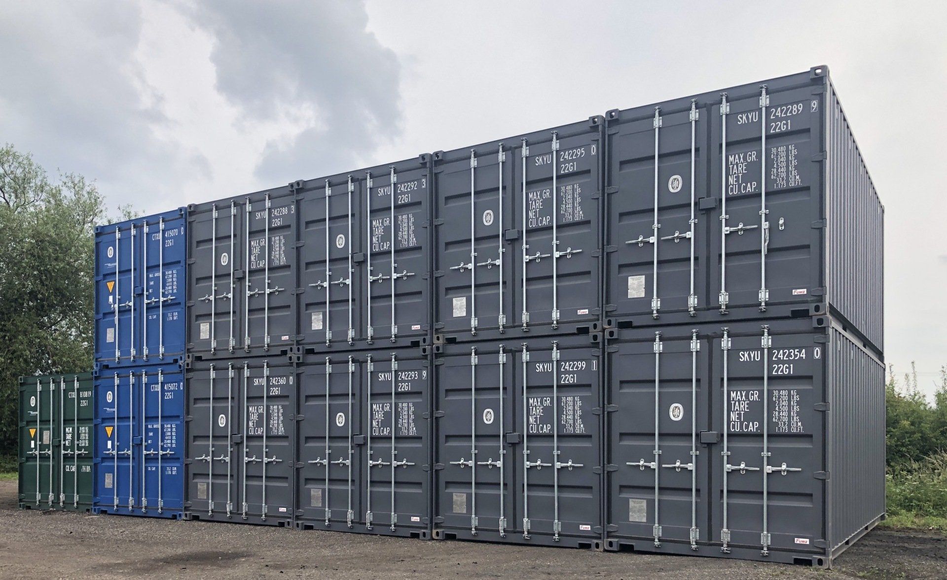 Stack of gray and blue shipping containers under a cloudy sky.