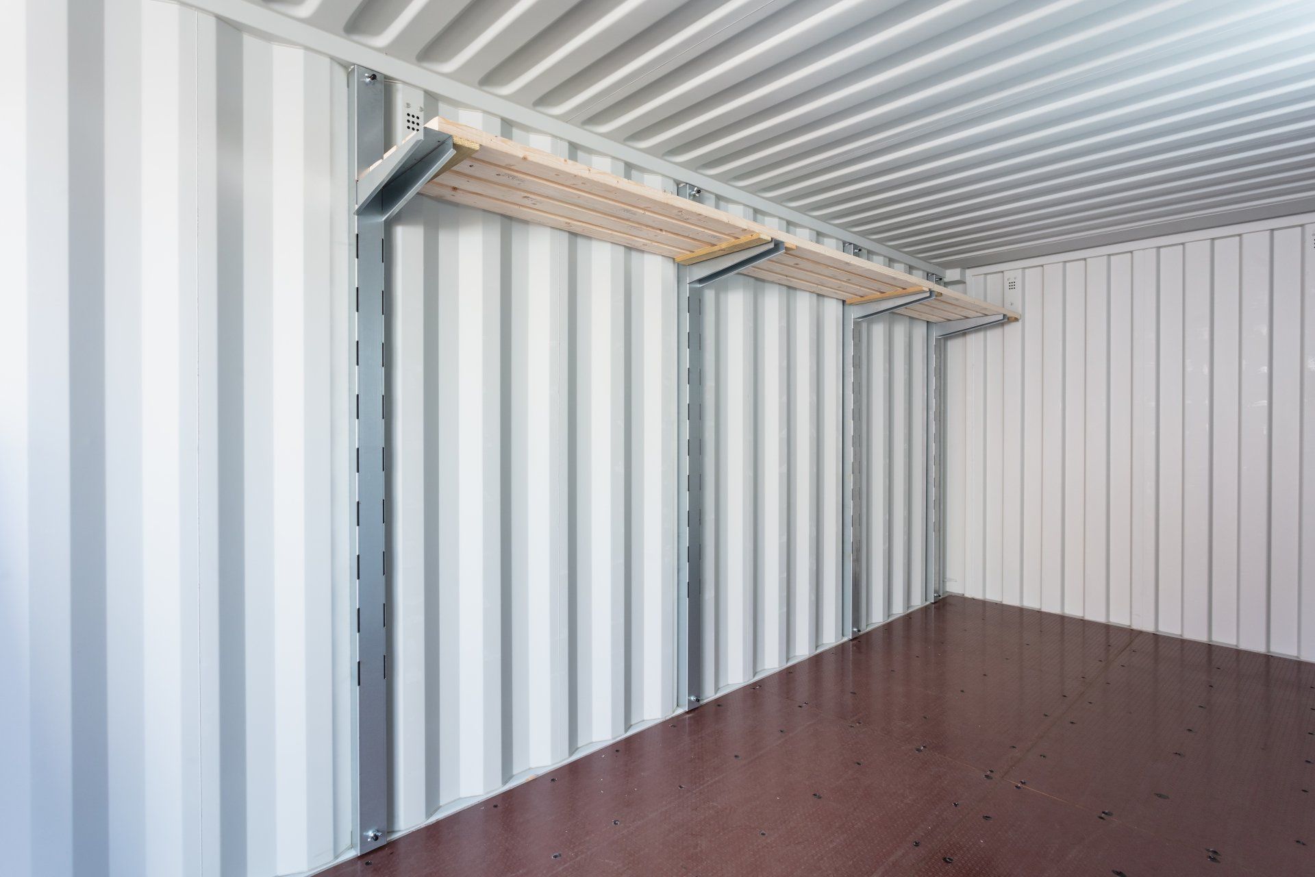 Empty, white interior of a storage container with shelving attached to the wall.