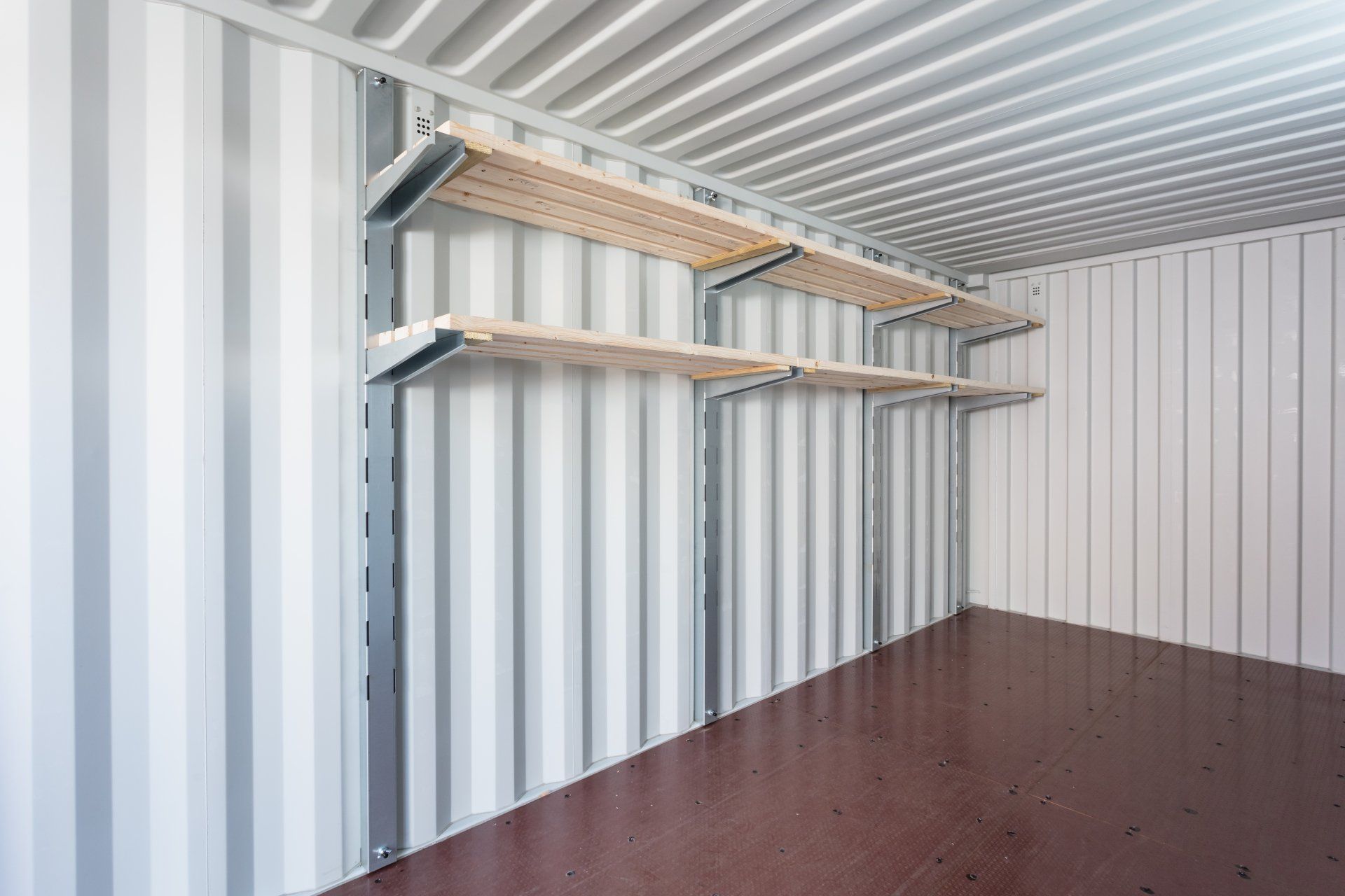 Empty storage container with shelves mounted on the wall; corrugated metal siding, wood shelves, and dark floor.