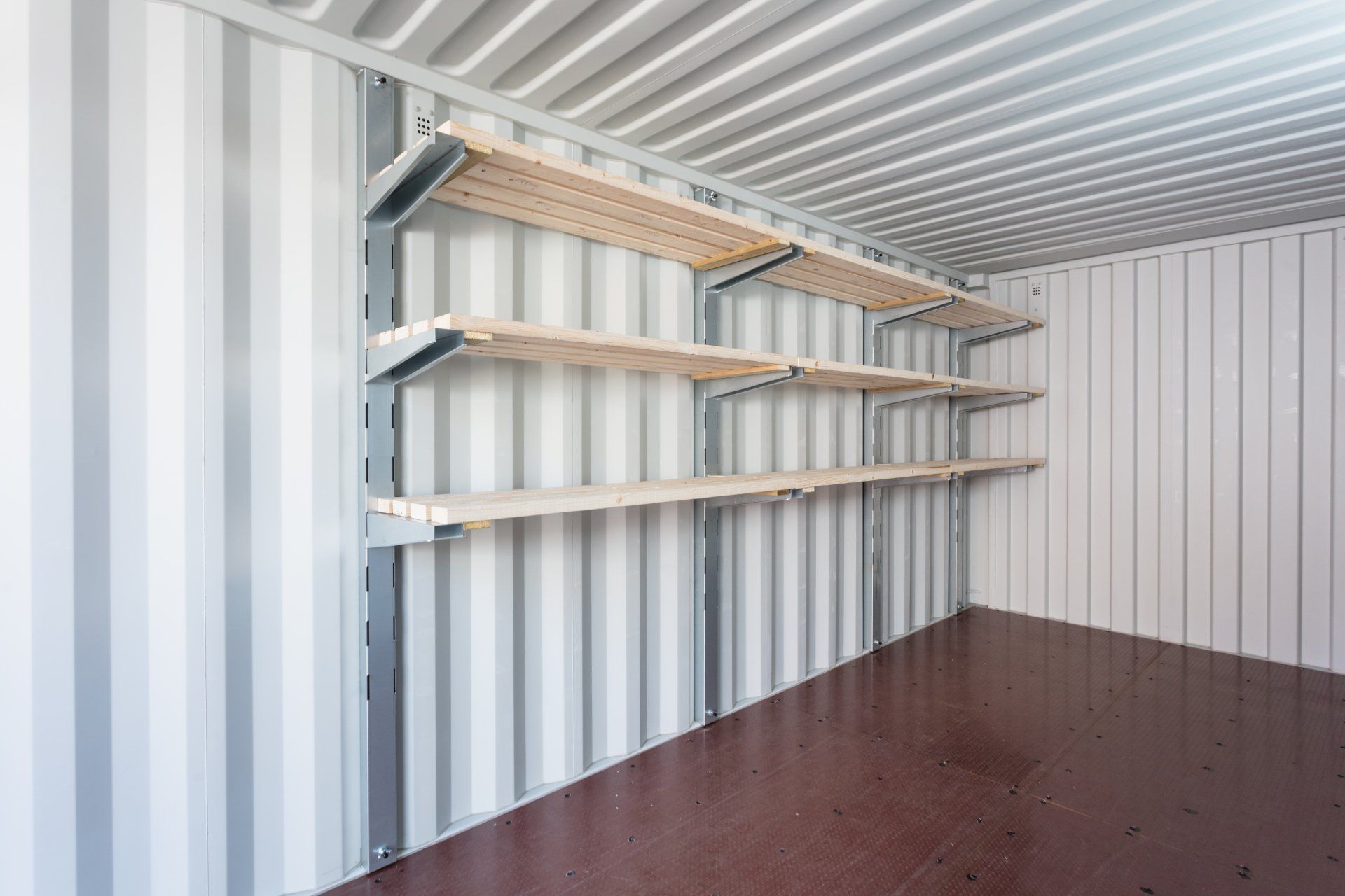 Empty cargo container with shelves mounted on one wall.