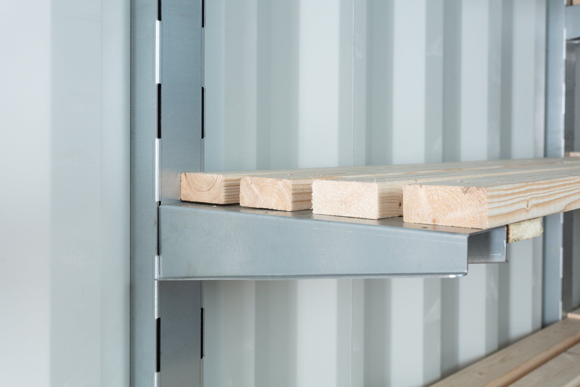 Close-up of shelving inside a gray storage container. Wooden planks rest on metal brackets.