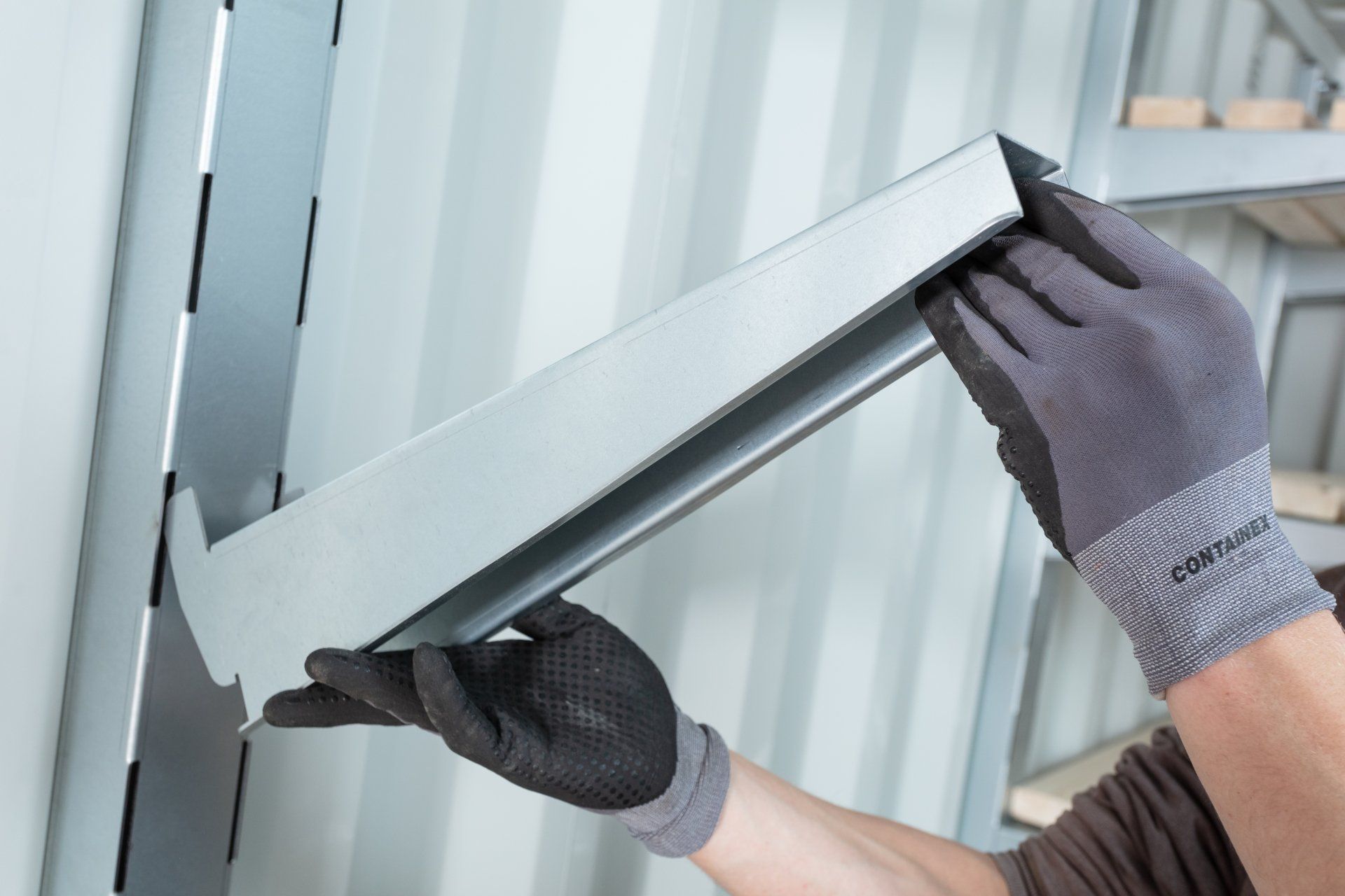Person wearing gloves installing a shelf bracket on a wall.