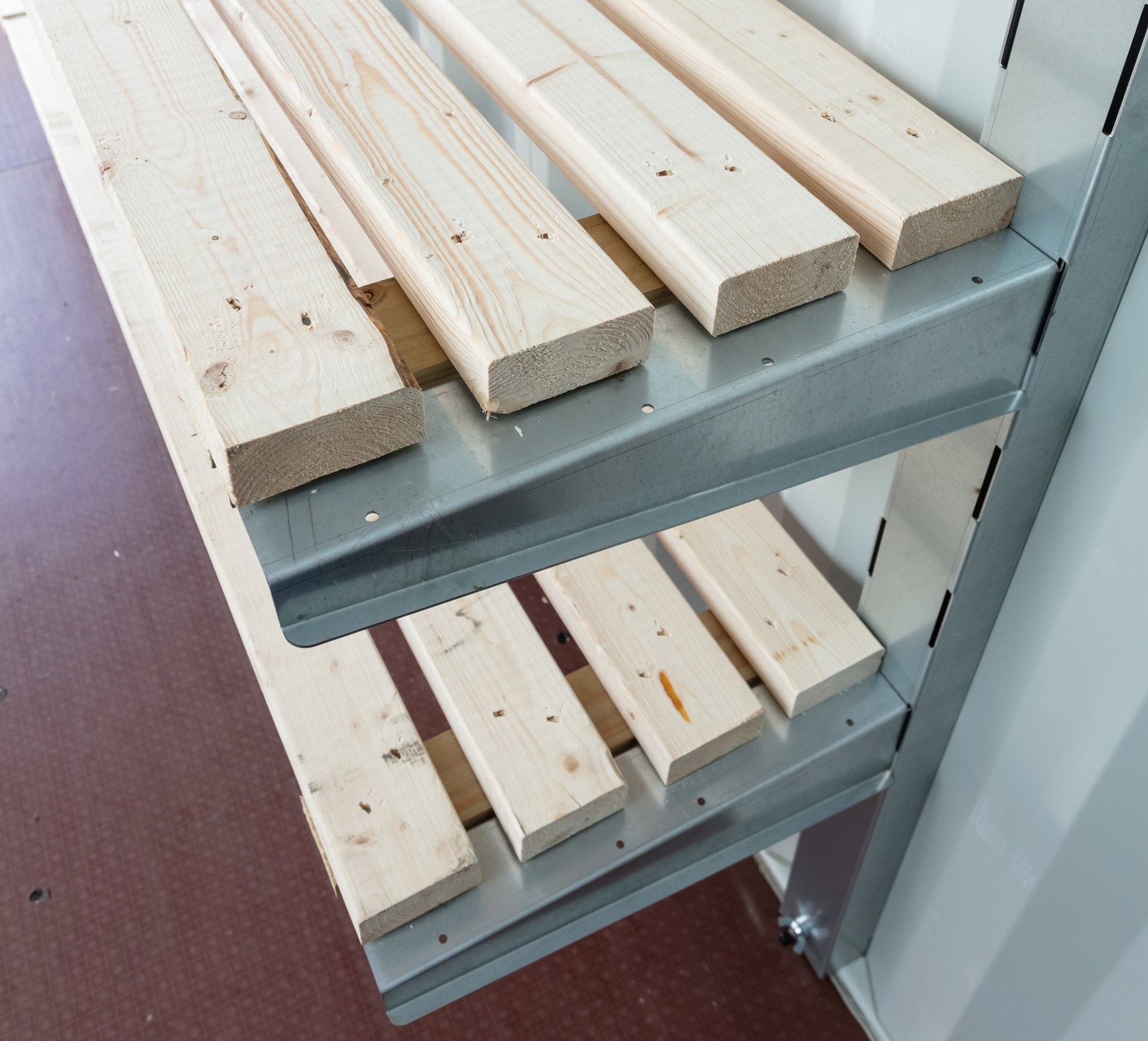 Three shelves holding stacks of wood boards inside a metal storage unit.