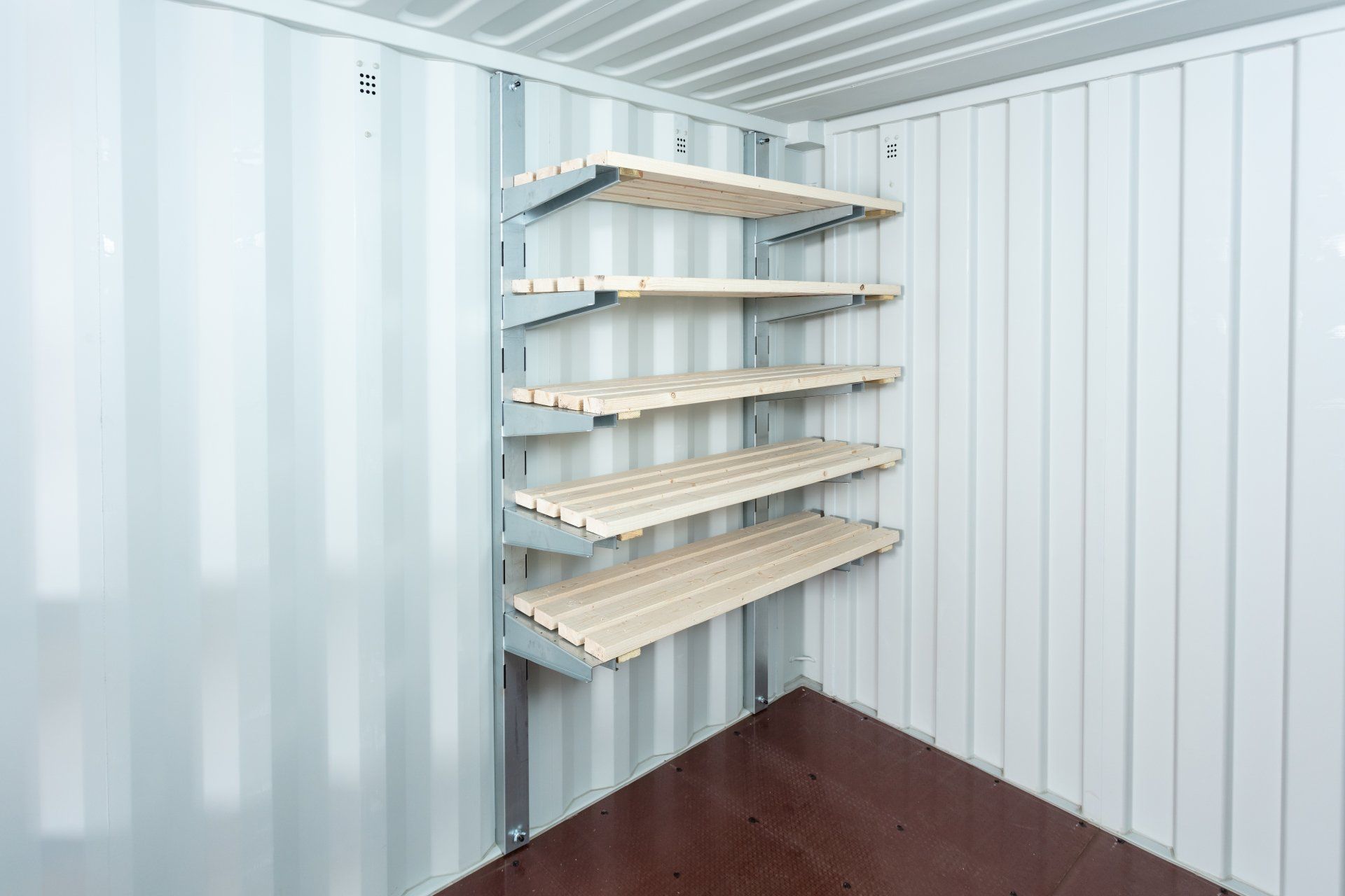 Shelves mounted on a corrugated white wall inside a white shipping container.