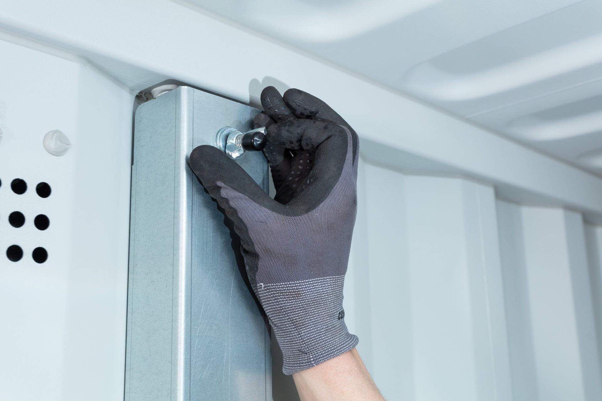 A gloved hand securing a bolt on a metal structure, likely for assembly or repair.