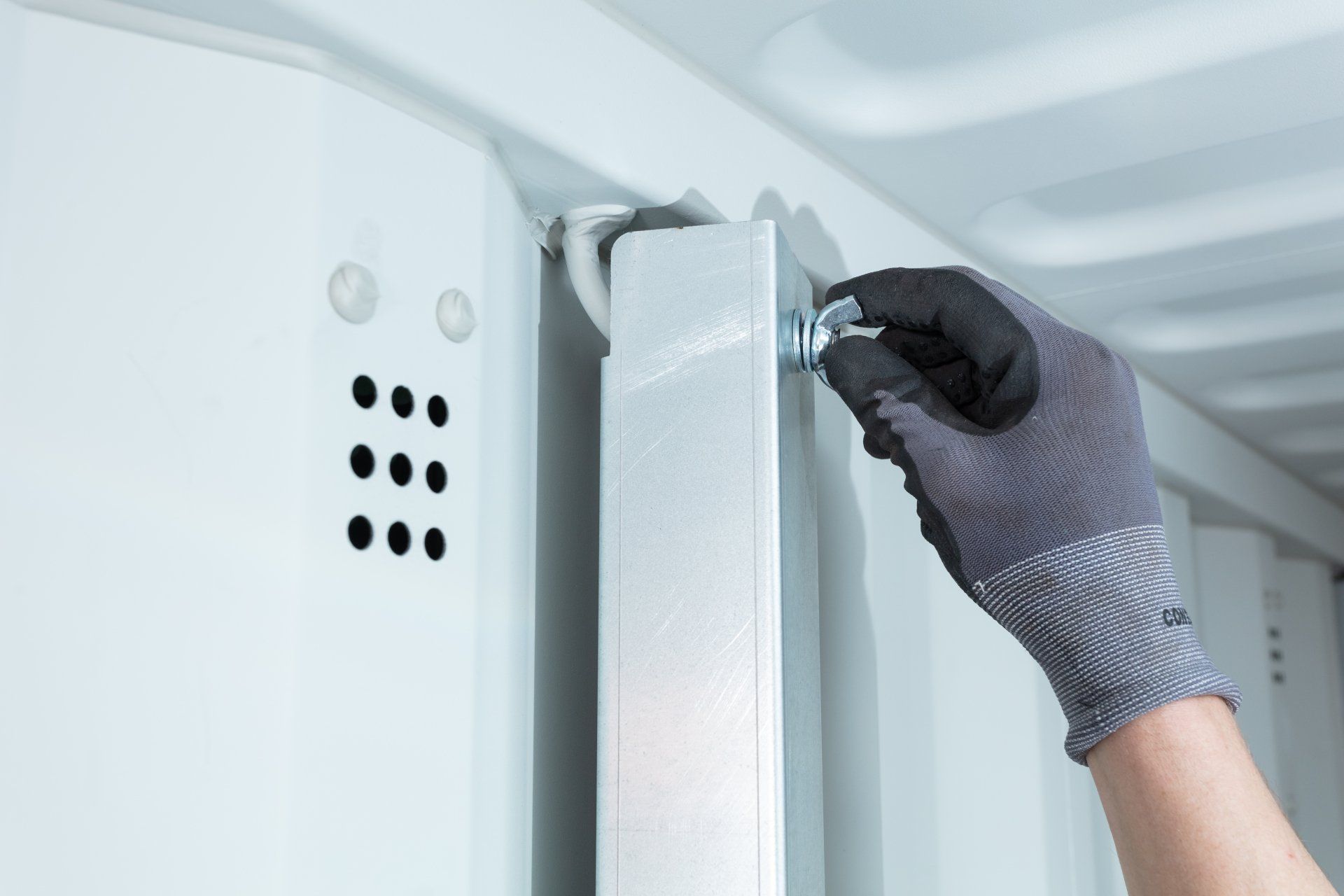Gloved hand tightening a bolt on a metal bar inside a white compartment.