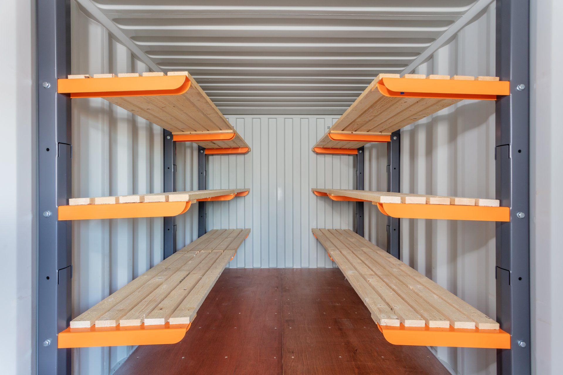 Shelving inside a metal container; orange metal brackets support wooden shelves.