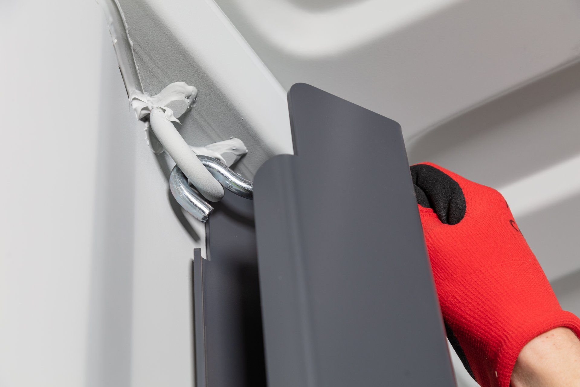 Gloved hand attaching a gray metal panel to a white surface using a clip and adhesive.