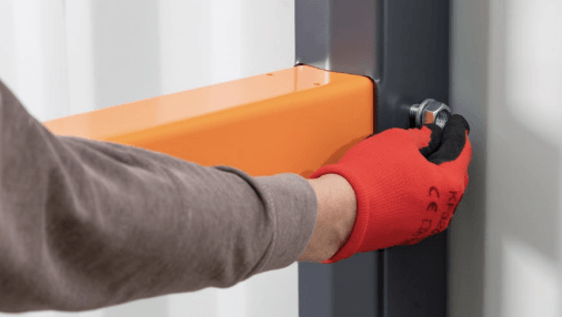 Person in red gloves tightening a bolt on an orange protective barrier attached to a black metal structure.