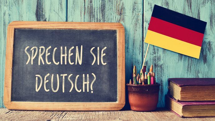 Chalkboard with “Sprechen Sie Deutsch?” beside a German flag, books, and a pencil cup on a rustic desk