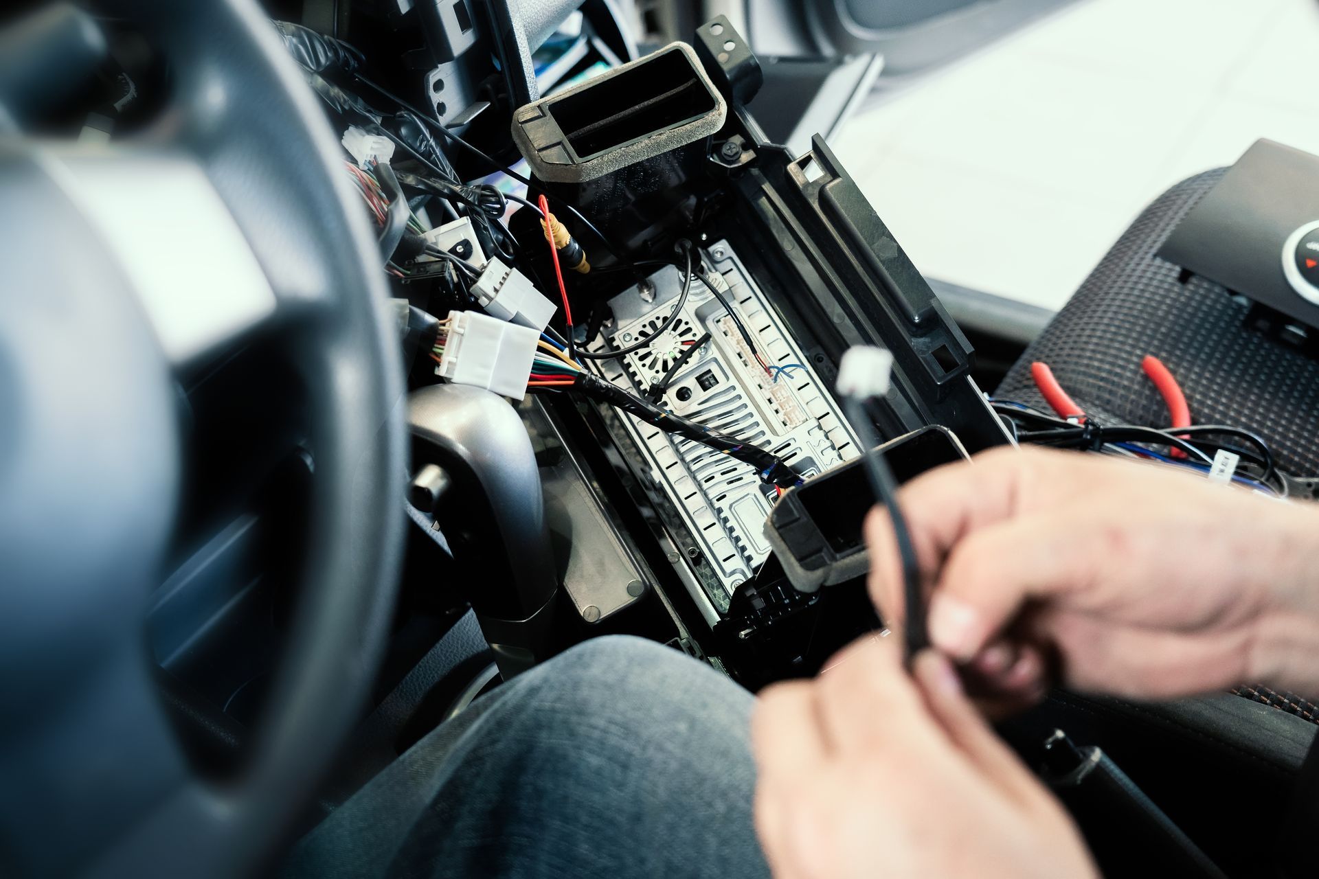 Hands working on a car dashboard wiring panel inside the vehicle.
