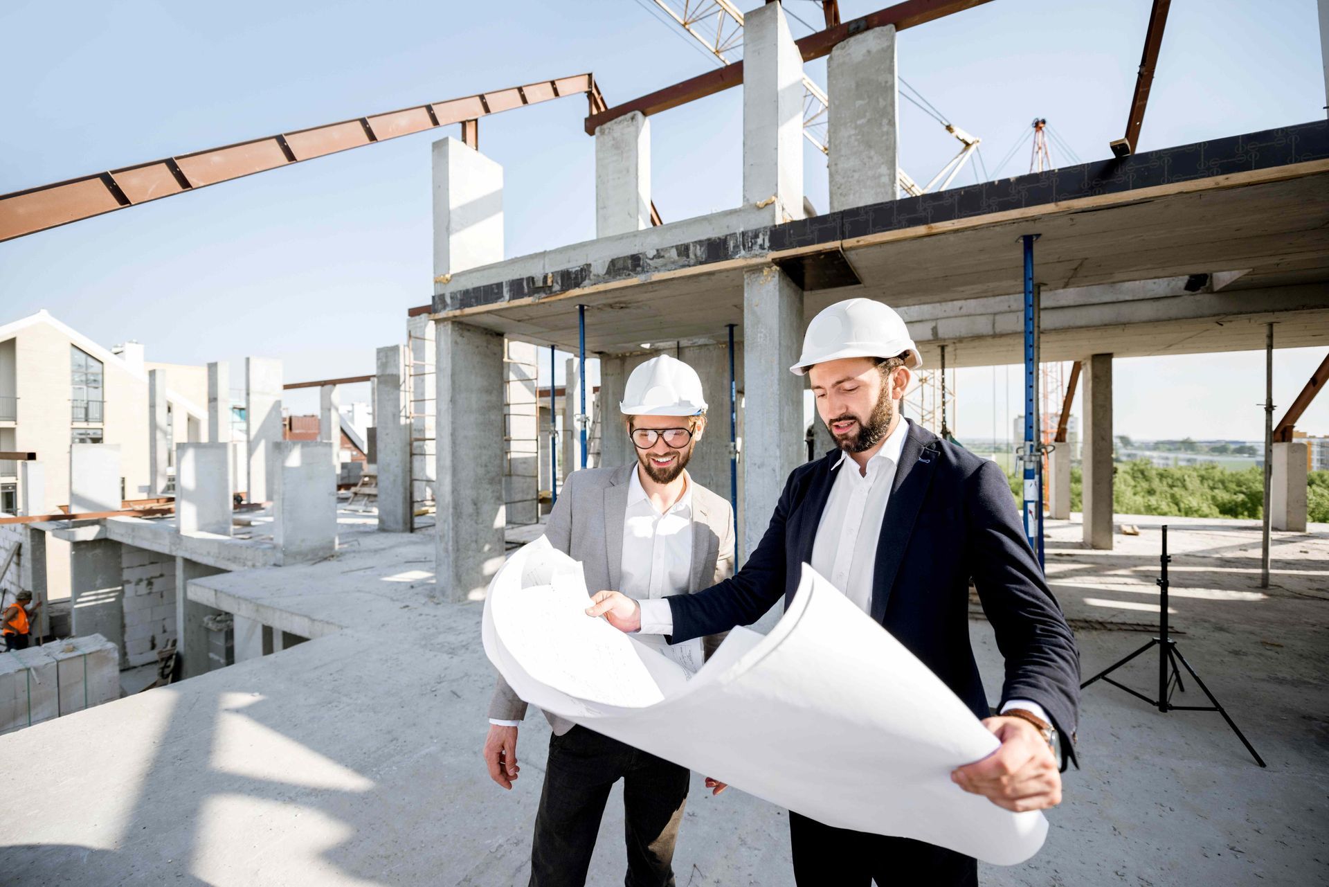 Two professionals in hard hats reviewing blueprints at an active construction site.