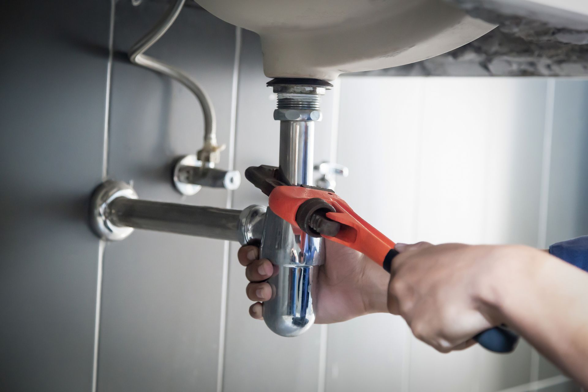 A plumber is fixing a sink pipe with a wrench.