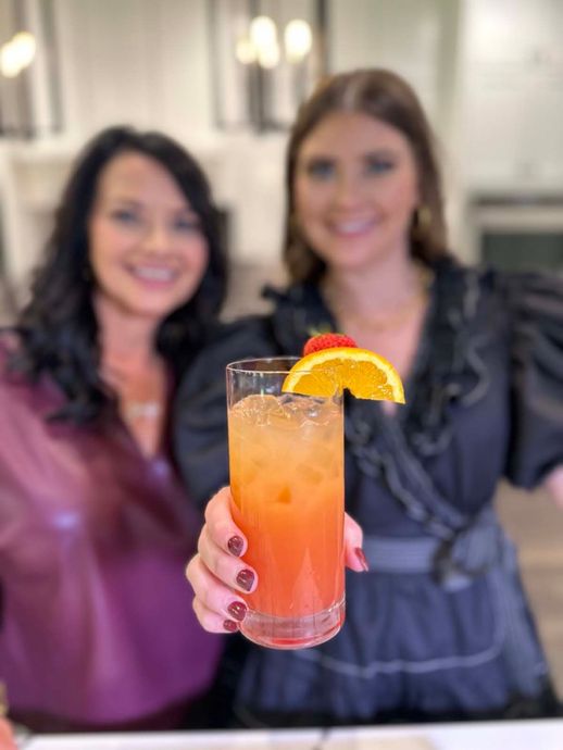 Two women are holding up a glass of orange juice.