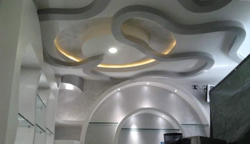 Soffitto interno moderno con pannelli bianchi ondulati e illuminazione a incasso calda sopra una porta ad arco.