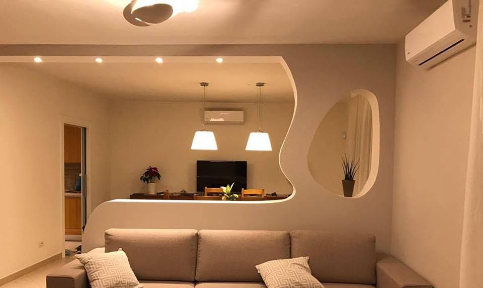 Soggiorno moderno con divano beige, apertura a muro verso la cucina e due lampade a sospensione.