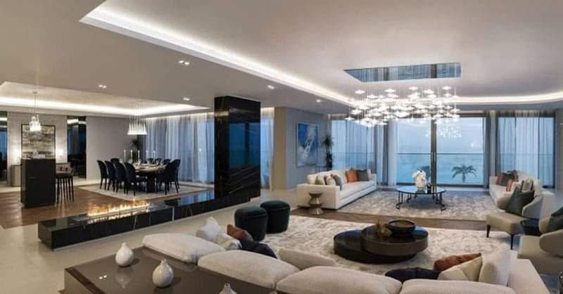 Soggiorno moderno e lussuoso con divani bianchi, eleganti dettagli neri, lampadario e finestre con vista sull'oceano.