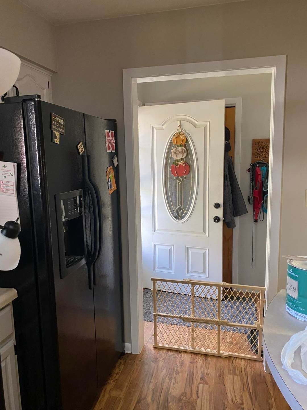 A black refrigerator stands next to an open doorway featuring a white door with an oval glass window and a wooden baby gate.
