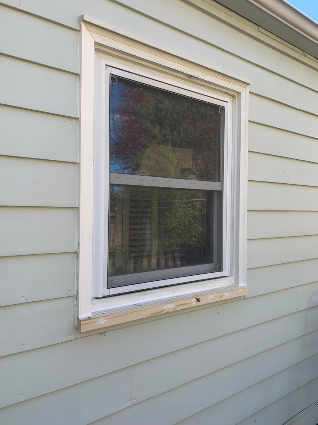 A white-framed window set into light green horizontal siding on the exterior of a house.