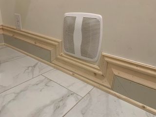 A wall-mounted HVAC vent cover set into cream-colored decorative baseboard molding above a marble-tiled floor.