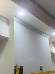 A white wall with crown molding near the ceiling, illuminated by recessed lighting, under construction.