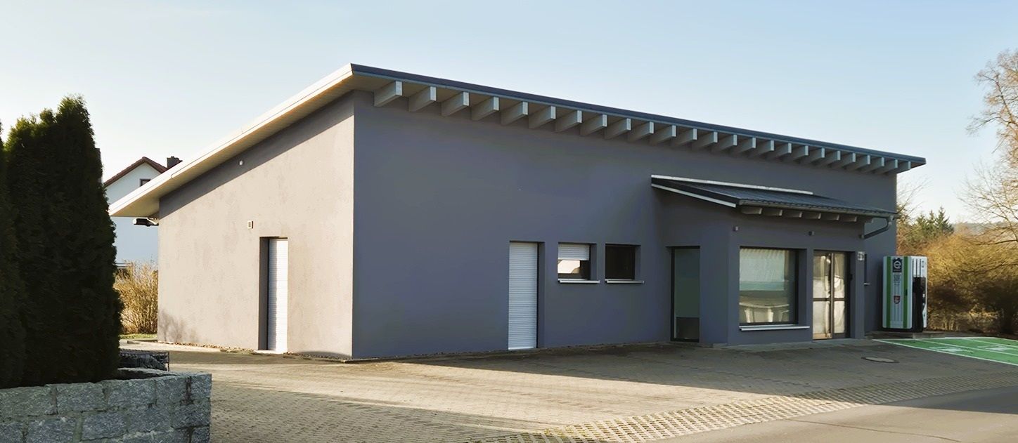 Modernes, eingeschossiges Haus mit grauen Wänden, großen Fenstern und einer Kiesauffahrt unter klarem Himmel