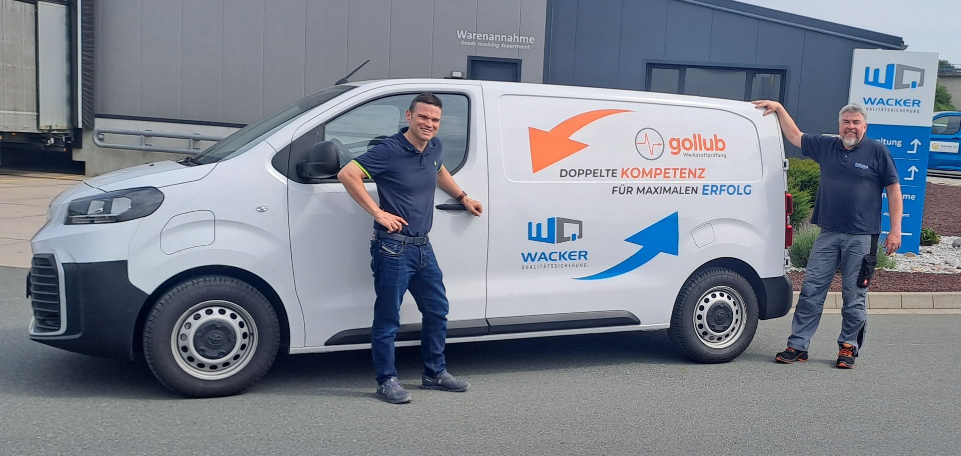 Zwei Männer stehen neben einem weißen Lieferwagen mit blau-orangenen Grafiken auf einem Industriegelände.