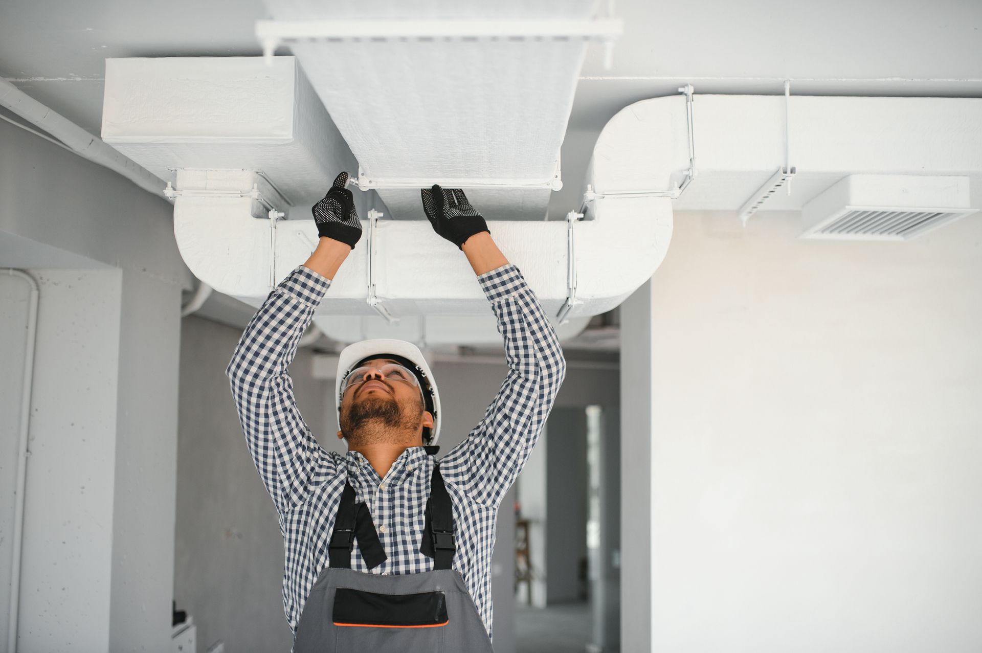 Worker wearing gloves inspects a ceiling HVAC vent in a bright room