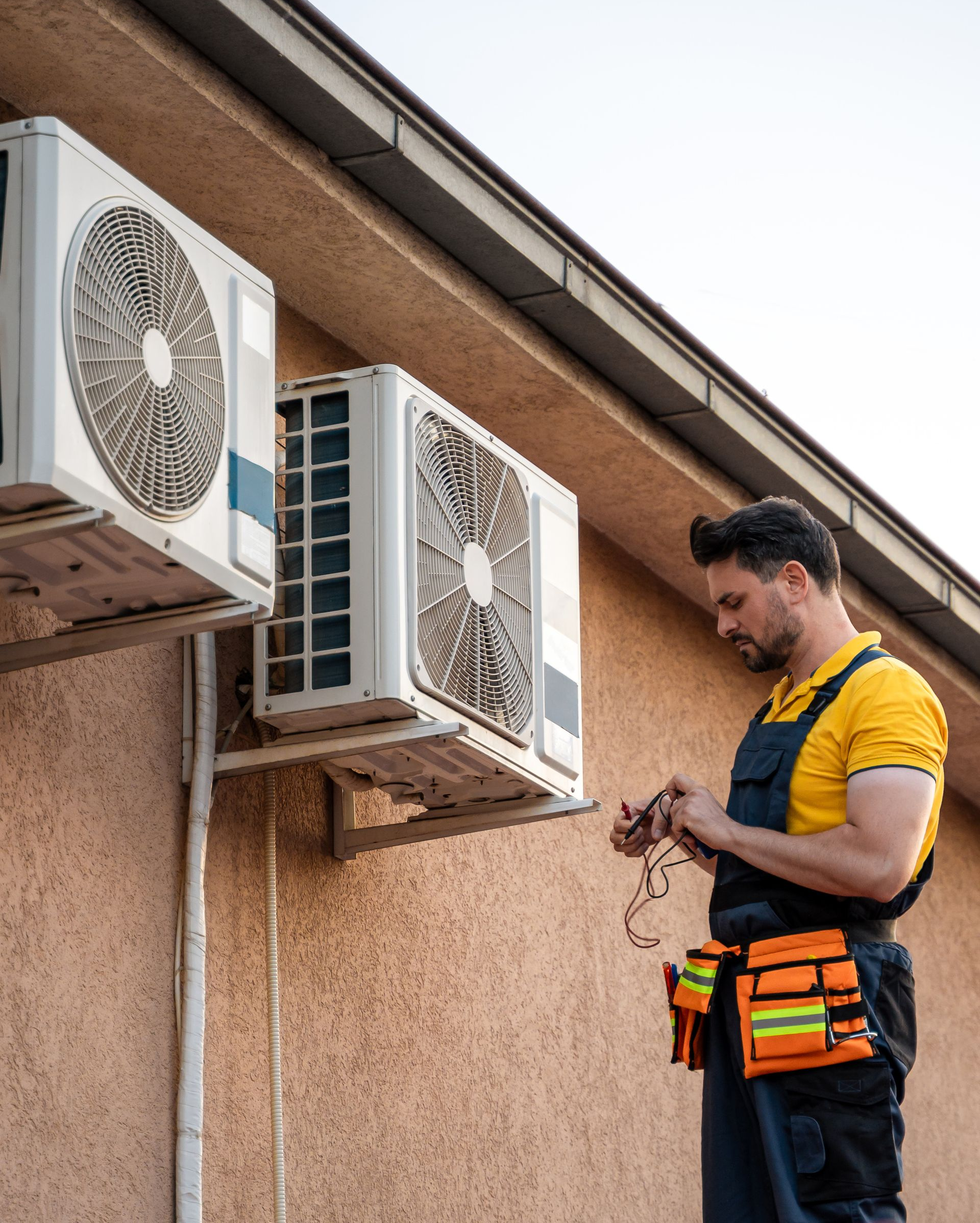 Technician with tools working on outdoor air conditioning units beside a building