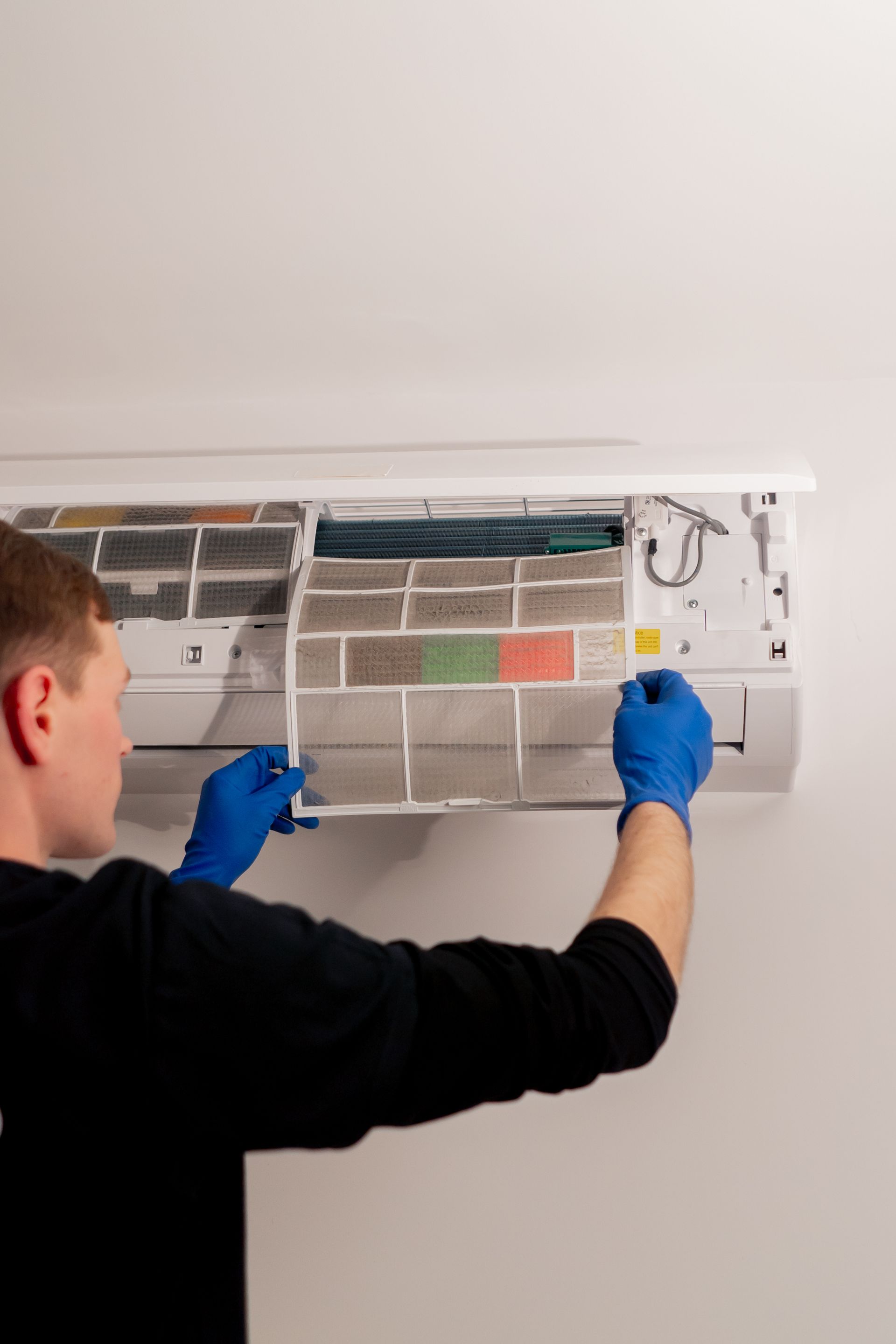 Technician cleaning a wall-mounted air conditioner filter with blue gloves