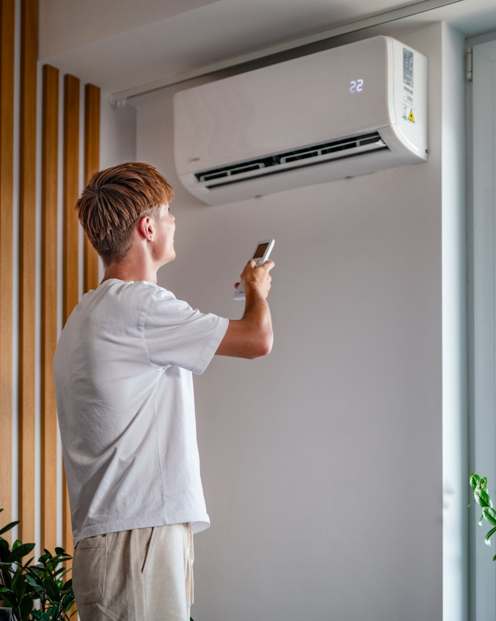 Person pointing a remote at a wall-mounted air conditioner in a modern room