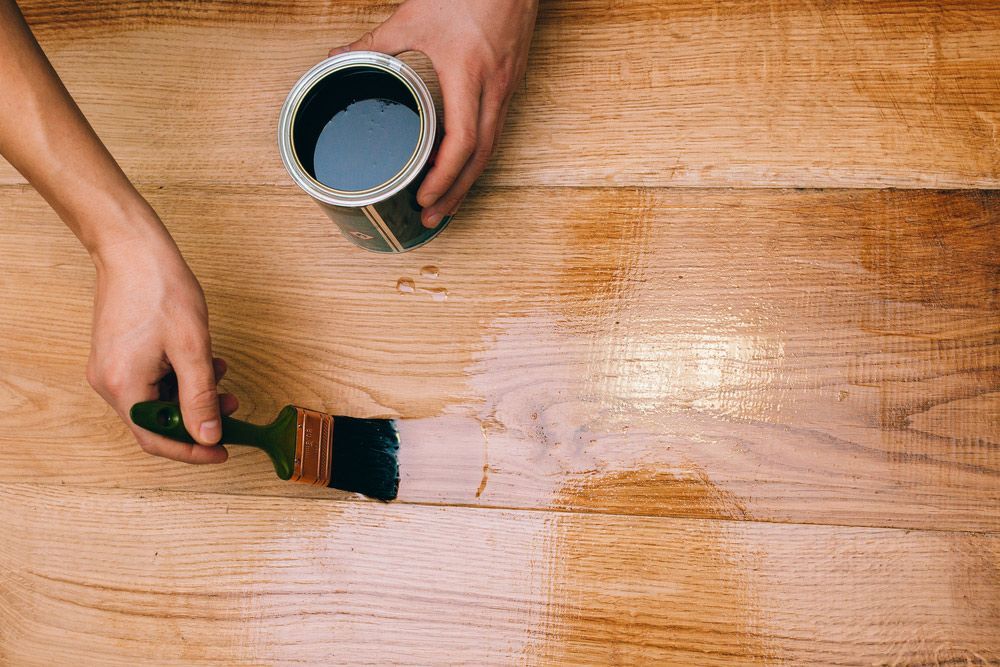 A Person is Painting a Wooden Table With a Brush — Timbertop Floor Sanding & Polishing In Cairns, QLD